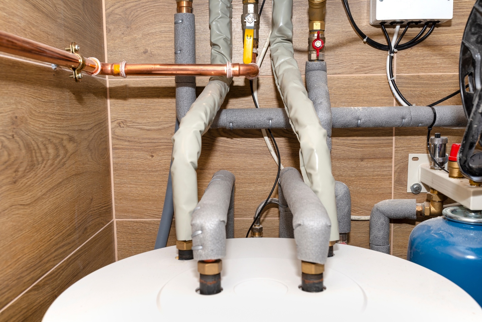 Water tank and gas pipes for a modern gas boiler in a home boiler room, lined with ceramic tiles.